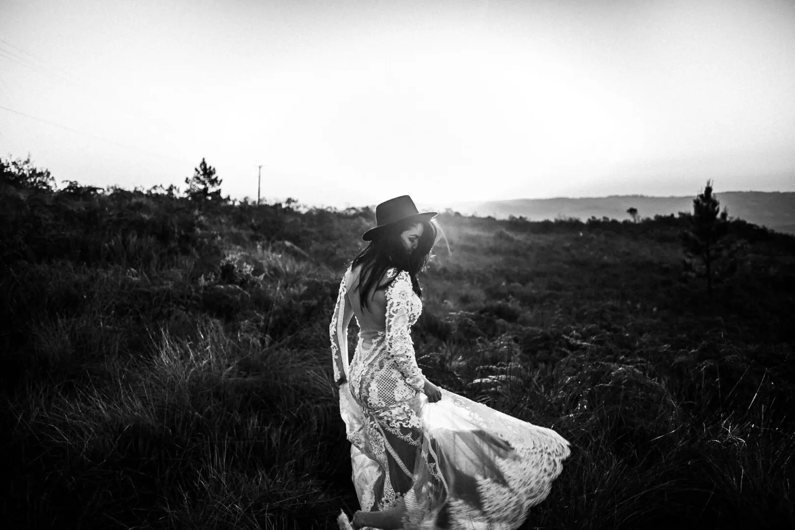 A woman in a hat and dress walking through the grass.