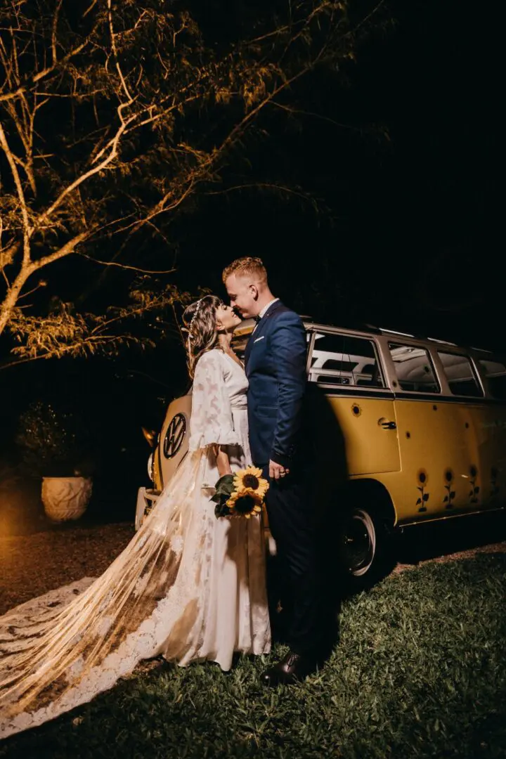 A man and woman kissing in front of a yellow van.