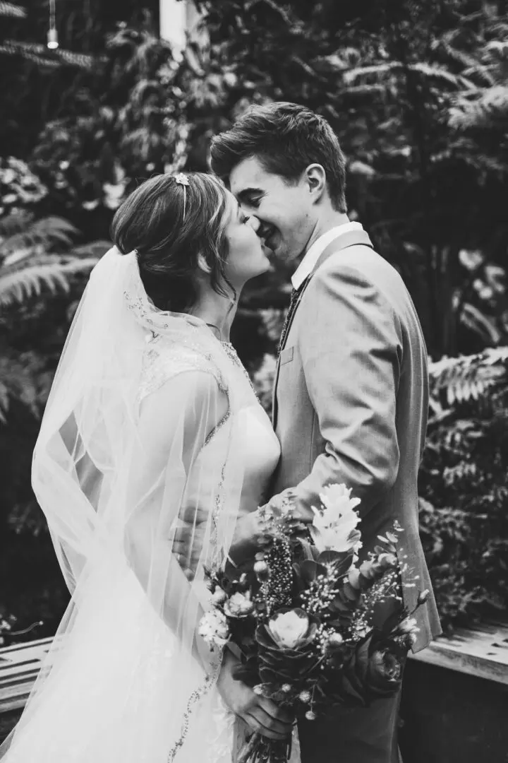 A man and woman kissing in front of trees.