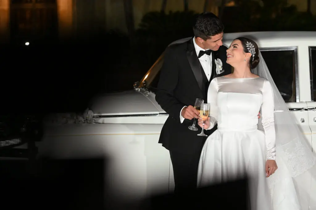 Happy newlyweds toasting by car.