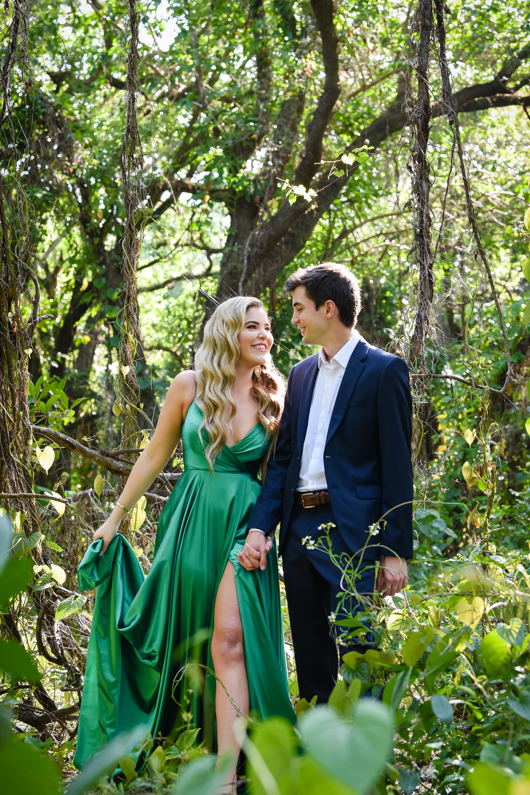 A man and woman in green dress walking through the woods.