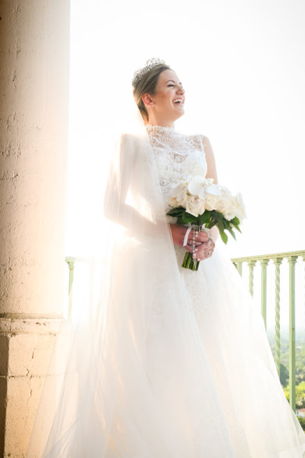 A bride holding her bouquet of flowers in front of the sun.