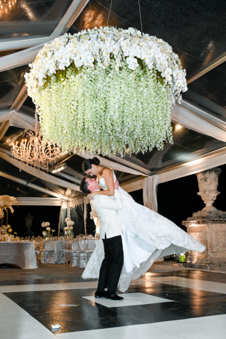 A bride and groom are dancing under the chandelier.