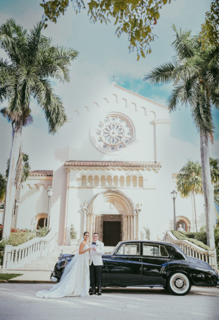A couple standing in front of a church with their limo.