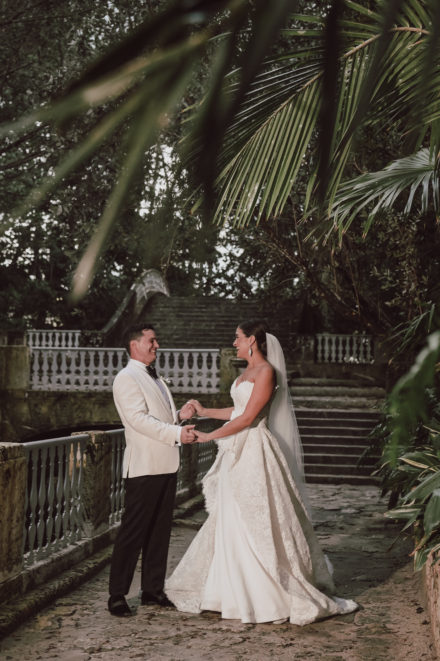 A bride and groom holding hands in front of palm trees.