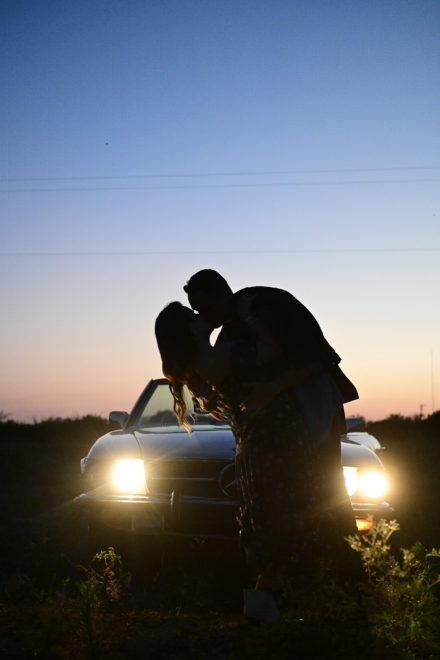 A man and woman kissing in front of a car.