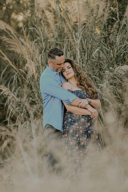 A man and woman hugging in tall grass.
