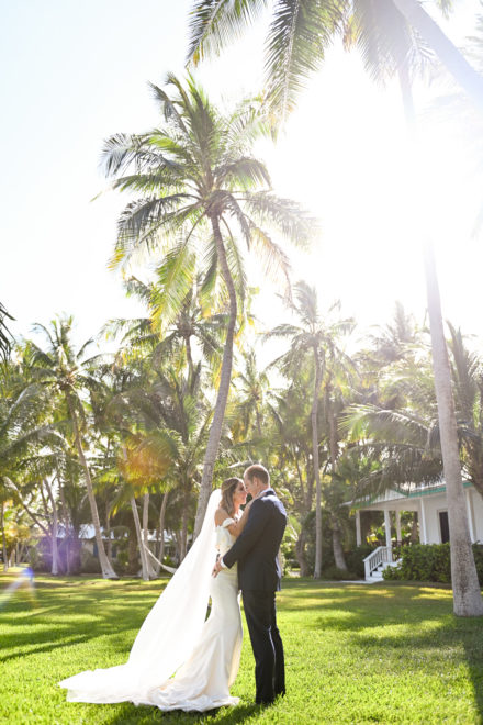 A bride and groom standing under the palm trees