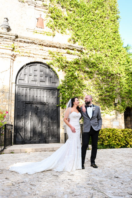 A bride and groom pose for a picture outside of the church.