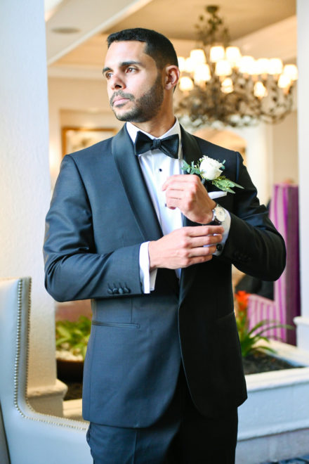 A man in a tuxedo holding onto a white rose.