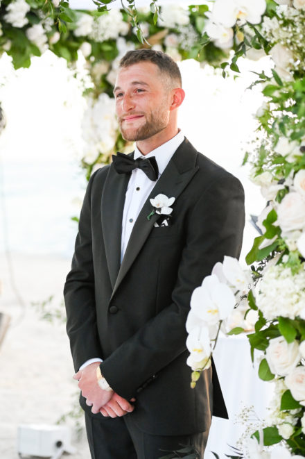 A man in a tuxedo standing next to flowers.