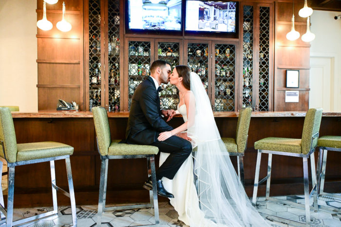 A bride and groom kissing in front of the bar.