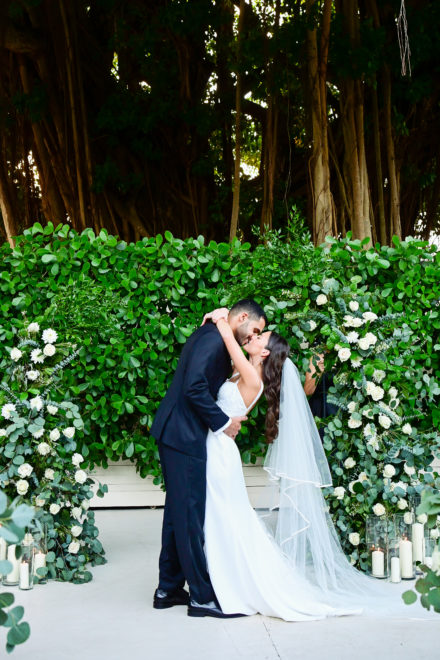 A bride and groom kissing in front of a hedge.