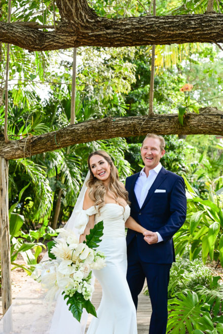 A bride and groom pose for a picture in front of a tree.
