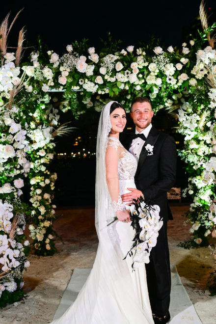 A bride and groom pose for a picture under an arch.