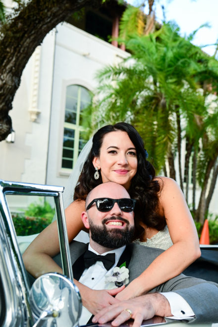 A bride and groom pose for the camera in their wedding car.