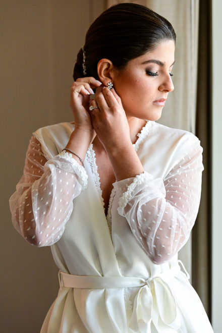 A woman in white robe putting on earrings.