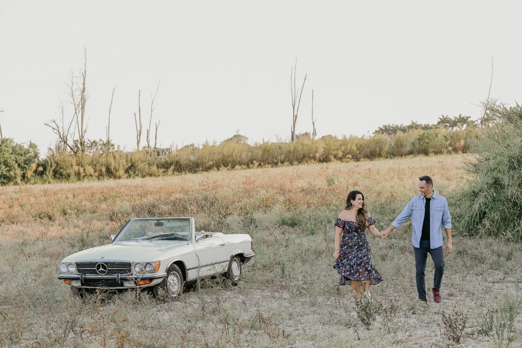 A man and woman holding hands in front of an old car.