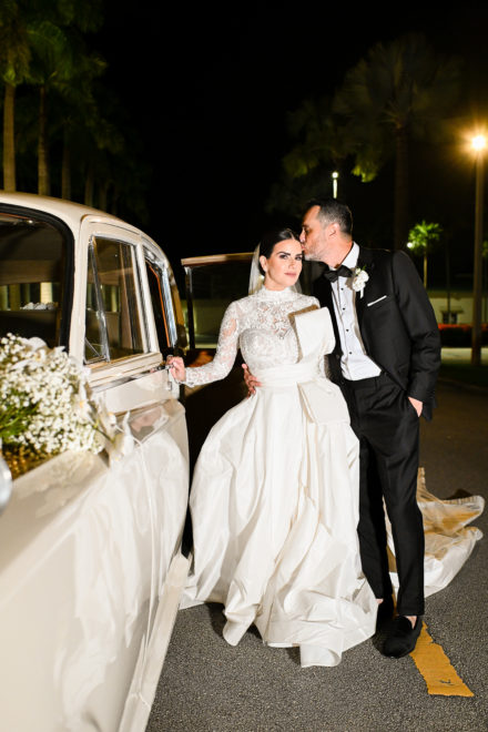 A bride and groom kissing in front of their wedding car.
