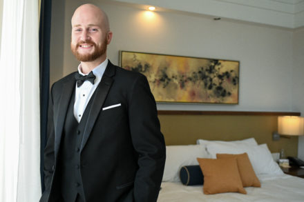 A man in a tuxedo standing next to a bed.