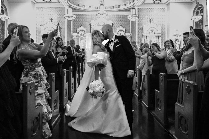 A bride and groom kissing in the aisle of a church.