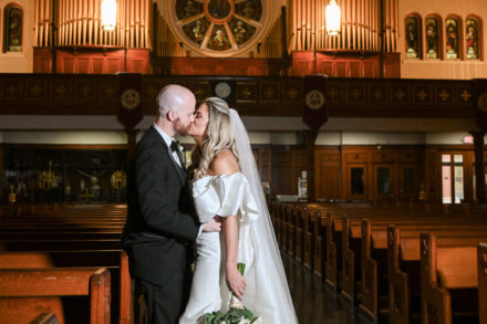 A bride and groom kissing in front of the pews.