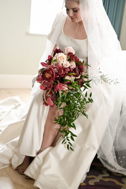A bride sitting on the ground holding her bouquet.