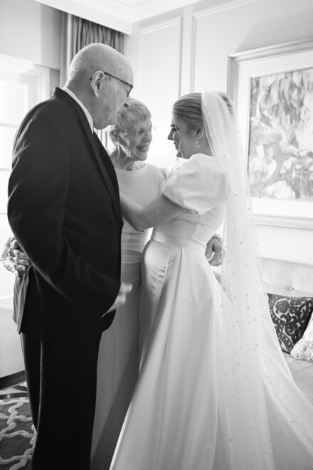A bride and groom are standing together in front of an older man.