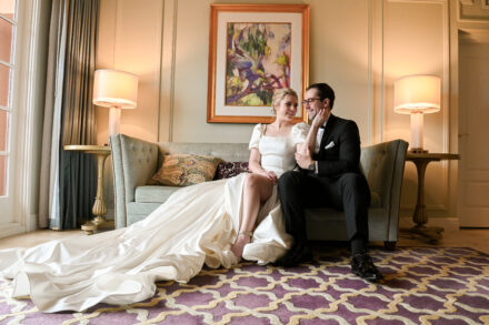 A bride and groom sitting on the couch in their wedding attire.