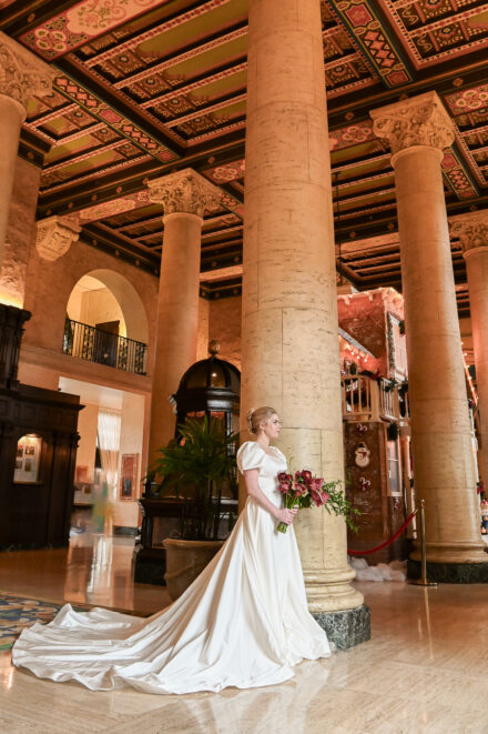 A woman in white dress holding flowers near pillars.