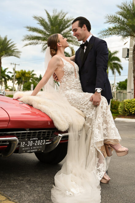 A bride and groom sitting on the hood of their car.