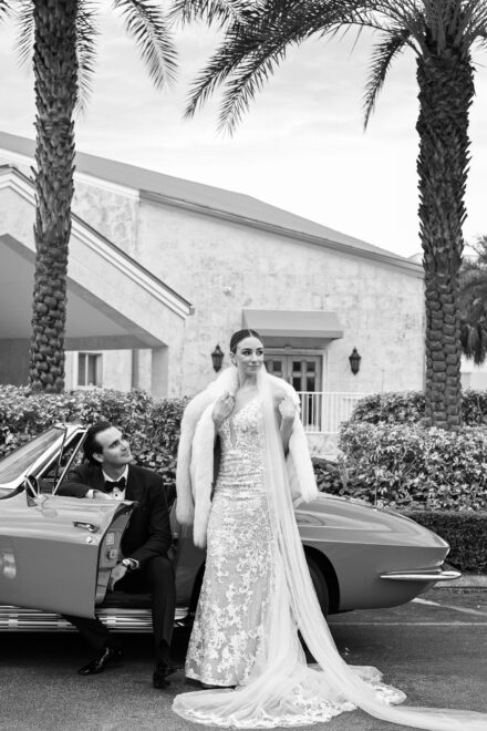 A man and woman in wedding dress standing next to car.
